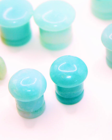 A beautifully fossilized pair of Ammonite Single Flare Plugs rests on a warm-toned background, showcasing the intricate spiral patterns of ancient marine life. Each plug is carefully carved from real ammonite fossils, revealing natural chambers in warm shades of caramel, amber, and deep brown, sometimes accented with hints of iridescent sheen. The surface is smoothly polished, allowing the fossil’s unique structure to shine through. Designed with a single flare and fitted with O-rings, these plugs offer a s