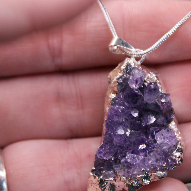 A beautiful Amethyst Pendant hangs gracefully from a sleek silver-color chain, combining natural elegance with everyday wearability. The pendant features a polished amethyst point or cabochon (style can vary), showcasing rich purple hues with subtle marbling or translucence that catches the light. Set in a simple metal cap or loop, the natural stone takes center stage. The silver-tone chain adds a modern, minimalist touch and pairs effortlessly with any outfit.