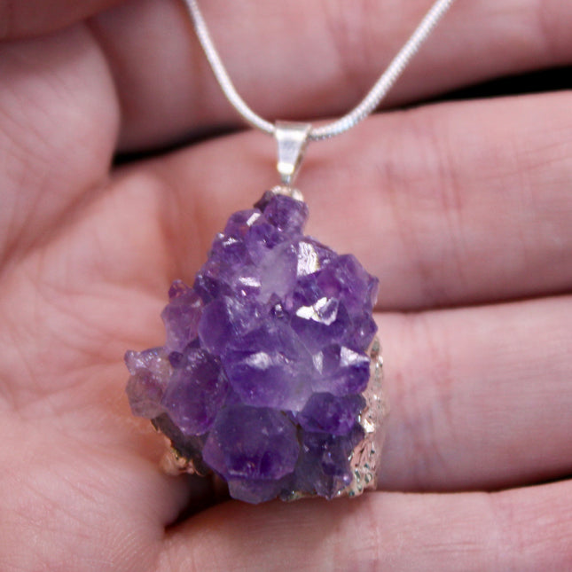 A beautiful Amethyst Pendant hangs gracefully from a sleek silver-color chain, combining natural elegance with everyday wearability. The pendant features a polished amethyst point or cabochon (style can vary), showcasing rich purple hues with subtle marbling or translucence that catches the light. Set in a simple metal cap or loop, the natural stone takes center stage. The silver-tone chain adds a modern, minimalist touch and pairs effortlessly with any outfit.