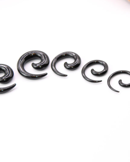 A pair of sleek, black acrylic spiral taper earrings displayed on a clean, neutral surface. The spirals curve smoothly in a bold, symmetrical design, tapering to fine points at the ends. Their glossy finish reflects light subtly, emphasizing their smooth texture and modern, minimalist style. Sized for stretched ears, the earrings showcase a striking balance of simplicity and statement, perfect for alternative or gauged jewelry wearers.