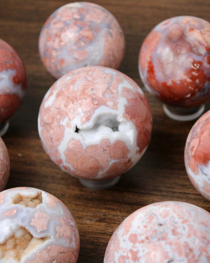 Elevate your space with the calming beauty and gentle energy of this hand-polished Flower Agate Sphere, a natural work of art that inspires peace, growth, and intention. Featuring dreamy shades of soft pink, creamy white, and warm peach, each sphere showcases unique floral-like inclusions that resemble delicate blooms suspended within the stone—making every piece truly one of a kind.
