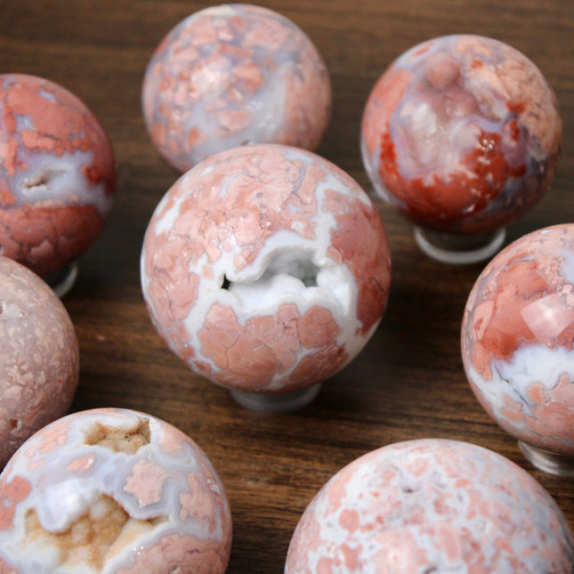 Elevate your space with the calming beauty and gentle energy of this hand-polished Flower Agate Sphere, a natural work of art that inspires peace, growth, and intention. Featuring dreamy shades of soft pink, creamy white, and warm peach, each sphere showcases unique floral-like inclusions that resemble delicate blooms suspended within the stone—making every piece truly one of a kind.