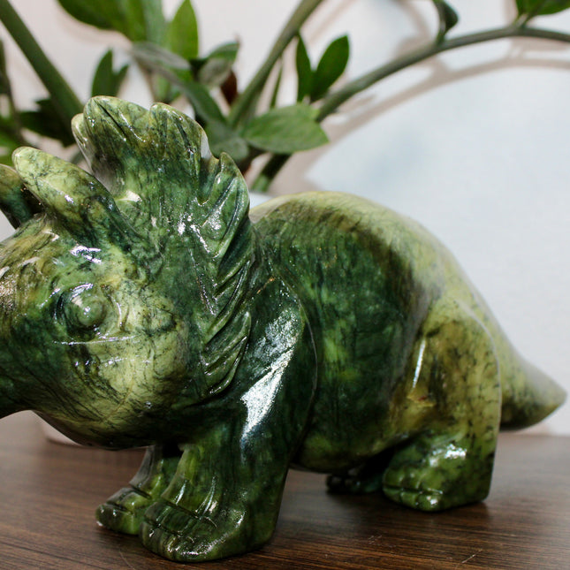 Green stone triceratops figurine on a wooden surface with plants in the background