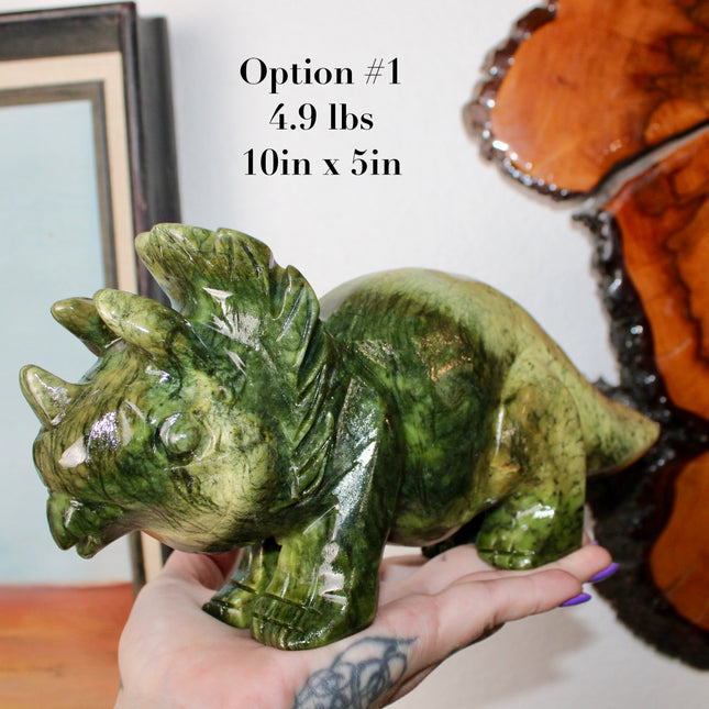 Green stone triceratops figurine on a wooden surface with plants in the background