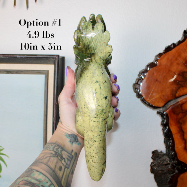 Green stone triceratops figurine on a wooden surface with plants in the background