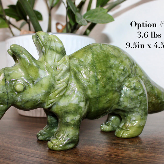 Green stone triceratops figurine on a wooden surface with plants in the background