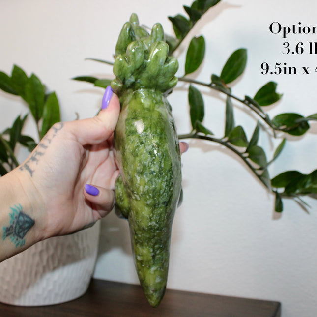 Green stone triceratops figurine on a wooden surface with plants in the background