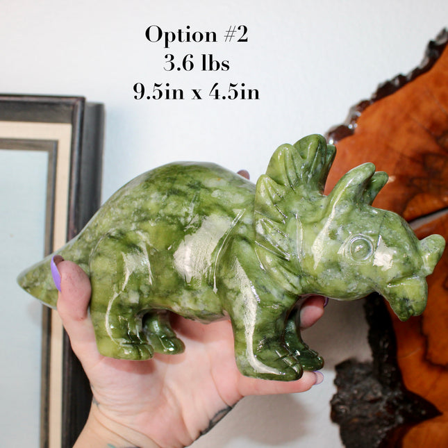 Green stone triceratops figurine on a wooden surface with plants in the background