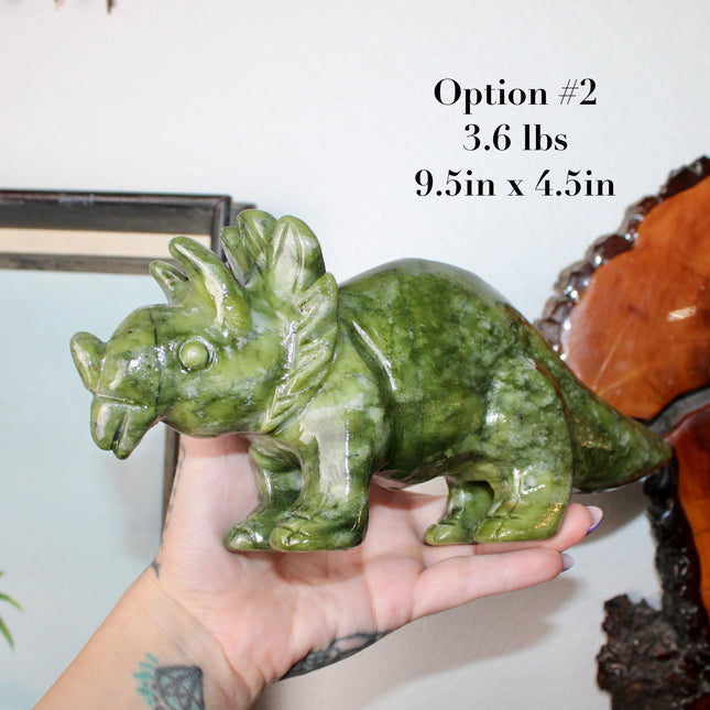 Green stone triceratops figurine on a wooden surface with plants in the background