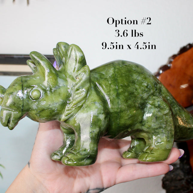 Green stone triceratops figurine on a wooden surface with plants in the background