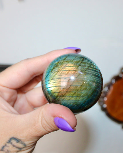 Hand holding a labradorite crystal ball with a blurred background