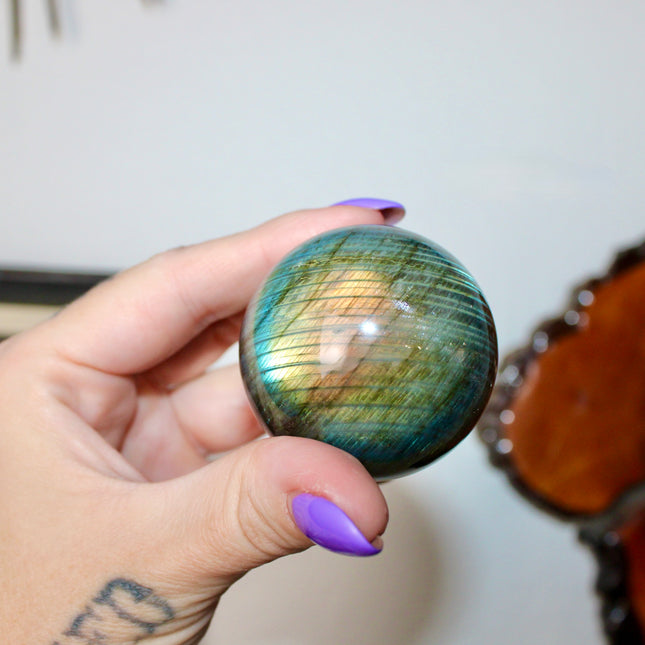 Hand holding a labradorite crystal ball with a blurred background
