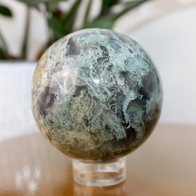 This XL Moss Agate Sphere features a stunning mix of natural green inclusions and cloudy white tones, reminiscent of forest landscapes or underwater gardens. Each sphere is one of a kind, with swirling patterns and depth that make it a true conversation piece.