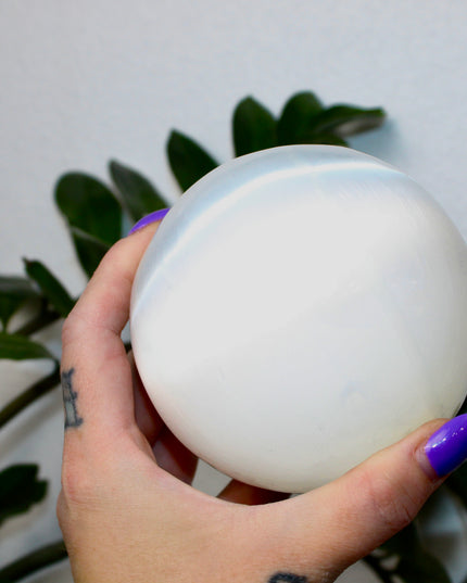 This XL Selenite Sphere showcases the luminous beauty of satin spar with its clean white tone and smooth, polished surface. Its generous size and soft glow make it a striking centerpiece for any space.