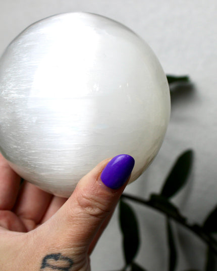 This XL Selenite Sphere showcases the luminous beauty of satin spar with its clean white tone and smooth, polished surface. Its generous size and soft glow make it a striking centerpiece for any space.