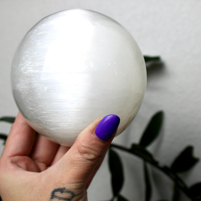 This XL Selenite Sphere showcases the luminous beauty of satin spar with its clean white tone and smooth, polished surface. Its generous size and soft glow make it a striking centerpiece for any space.