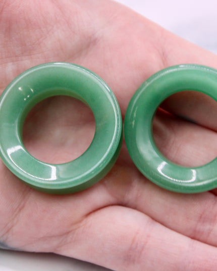 Two green jade tunnel plugs held in a hand against a neutral background