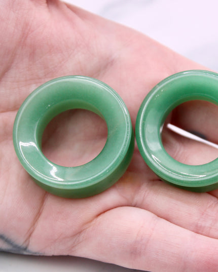 Two green jade tunnel plugs held in a hand against a white background