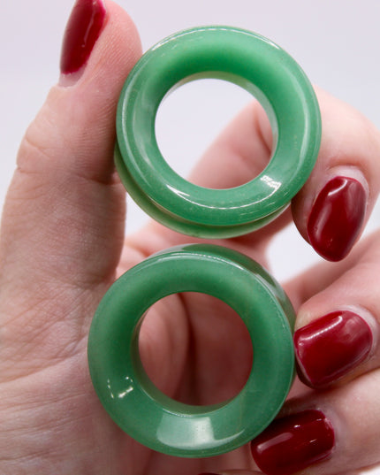 Green tunnel plugs jade green aventurine held in a hand with red nail polish on a white background