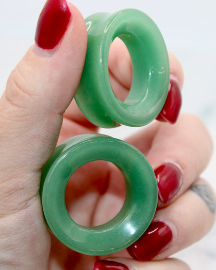 Green jade tunnel plugs held by a hand with red nail polish on a white background