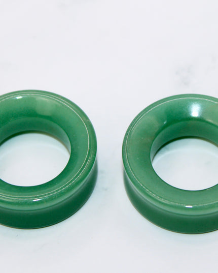 Two green aventurine tunnel plugs on a white marble surface