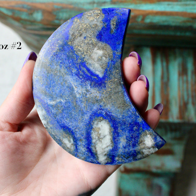 Crescent-shaped blue lapis held by a hand with text indicating size and option.