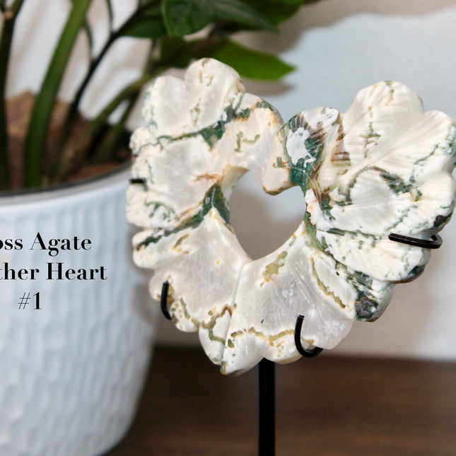 Bring nature’s elegance into your space with this one-of-a-kind Moss Agate Heart Feather Carving on Stand. Each piece is intricately carved into a heart-shaped feather design, capturing soft, organic curves that symbolize both love and lightness. Made from genuine Moss Agate, these carvings showcase lush, forest-like inclusions of deep green within a translucent to milky white base—every piece with its own unique pattern, just like nature intended.