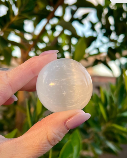 Hand holding a clear crystal ball with a blurred green outdoor background