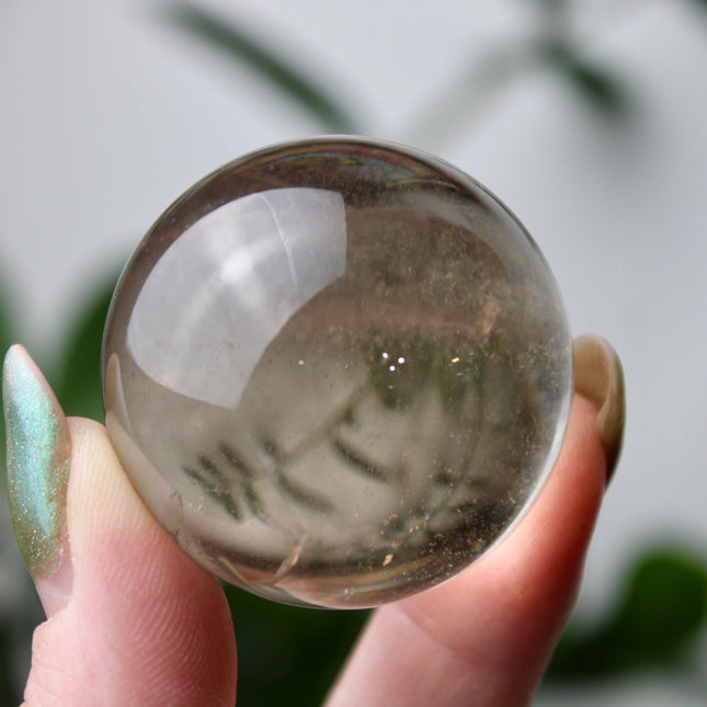 High grade genuine smoky quartz crystal sphere with natural clarity in deep translucent brown to smoky gray tones, hand-polished and displayed on a sturdy silver stand – grounding crystal for meditation, energy clearing, and root chakra healing