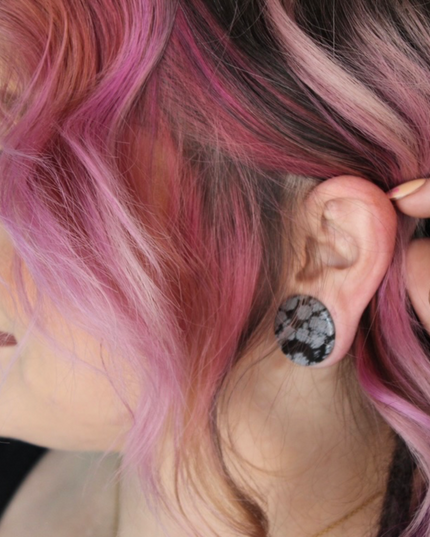 These Snowflake Obsidian Double Flared Plugs feature a smooth, polished surface with natural gray-white crystal "snowflakes" scattered across a rich black volcanic glass base. The double flare ensures a secure, comfortable fit for stretched ears without the need for O-rings. Each pair is uniquely patterned, showcasing the stone’s natural beauty and grounding energy. Durable and stylish, these plugs add a bold yet refined touch to any stretched ear jewelry collection.