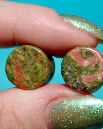 A grounded and vibrant pair of Unakite Double Flare Stone Plugs is displayed on a textured natural background. Each plug showcases the stone’s distinctive blend of mossy green epidote and soft, salmon-pink feldspar—creating a one-of-a-kind marbled pattern that feels both earthy and energizing. The smooth, hand-polished finish enhances the natural contrast in the stone’s texture and color. With a double flare shape for secure, comfortable wear, these plugs combine style with the natural, balancing energy Una