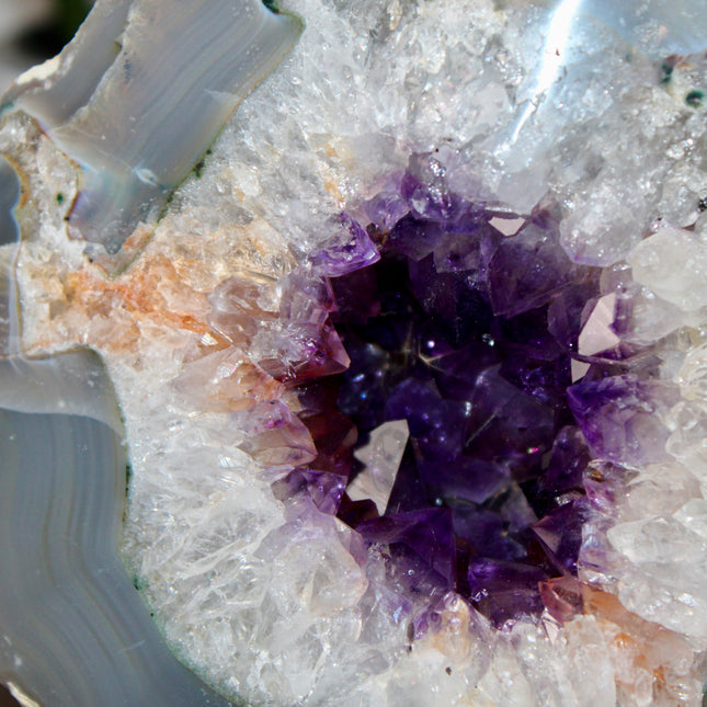 An impressive Large Geode stands tall on its included display stand, revealing a breathtaking Grade A Dark Purple Amethyst Druzy Center. The interior is densely lined with sparkling amethyst crystals, rich in deep violet tones and glowing with natural brilliance. The druzy surface catches the light with every angle, creating a glittering effect that highlights the exceptional clarity and saturation of the crystals. The raw outer shell offers a rugged, earthy contrast to the radiant core, emphasizing the geo