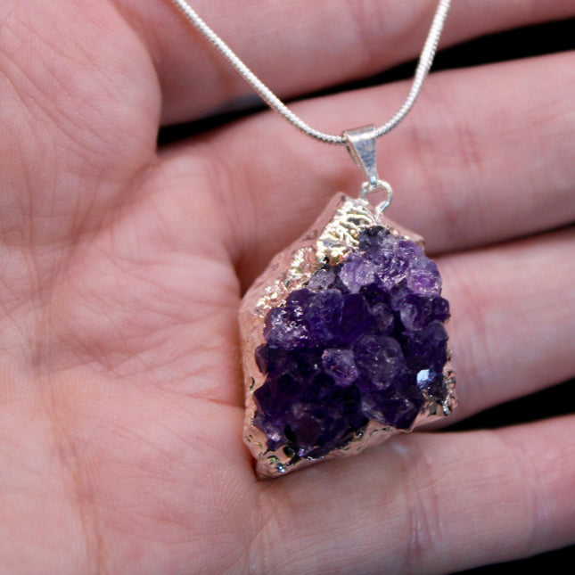 A beautiful Amethyst Pendant hangs gracefully from a sleek silver-color chain, combining natural elegance with everyday wearability. The pendant features a polished amethyst point or cabochon (style can vary), showcasing rich purple hues with subtle marbling or translucence that catches the light. Set in a simple metal cap or loop, the natural stone takes center stage. The silver-tone chain adds a modern, minimalist touch and pairs effortlessly with any outfit.