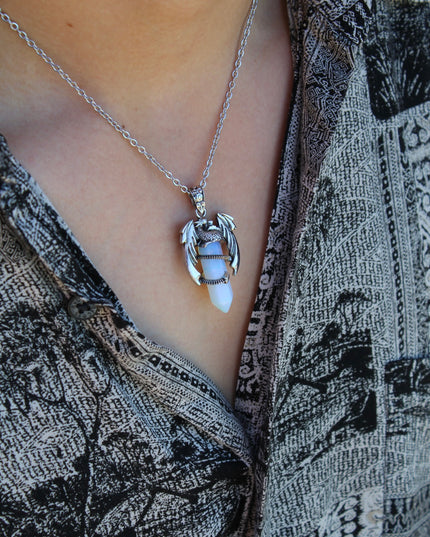 A fierce and enchanting Dragon Necklace with Opalite brings fantasy to life, featuring a detailed dragon wrapped protectively around a glowing opalite orb. The iridescent stone shimmers with soft hues of blue, lavender, and pearly white, catching light with a mystical glow. The dragon pendant is crafted with intricate scales and wings, giving it a bold, medieval-inspired aesthetic.