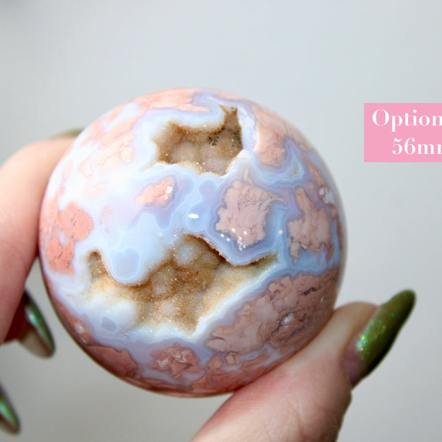Elevate your space with the calming beauty and gentle energy of this hand-polished Flower Agate Sphere, a natural work of art that inspires peace, growth, and intention. Featuring dreamy shades of soft pink, creamy white, and warm peach, each sphere showcases unique floral-like inclusions that resemble delicate blooms suspended within the stone—making every piece truly one of a kind.