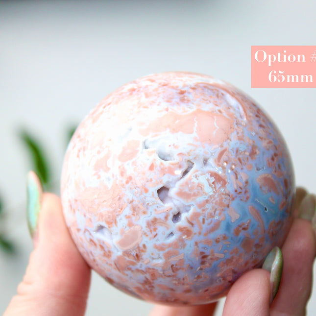 Elevate your space with the calming beauty and gentle energy of this hand-polished Flower Agate Sphere, a natural work of art that inspires peace, growth, and intention. Featuring dreamy shades of soft pink, creamy white, and warm peach, each sphere showcases unique floral-like inclusions that resemble delicate blooms suspended within the stone—making every piece truly one of a kind.