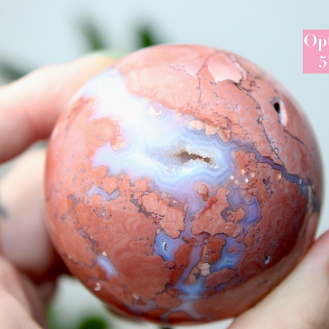 Elevate your space with the calming beauty and gentle energy of this hand-polished Flower Agate Sphere, a natural work of art that inspires peace, growth, and intention. Featuring dreamy shades of soft pink, creamy white, and warm peach, each sphere showcases unique floral-like inclusions that resemble delicate blooms suspended within the stone—making every piece truly one of a kind.