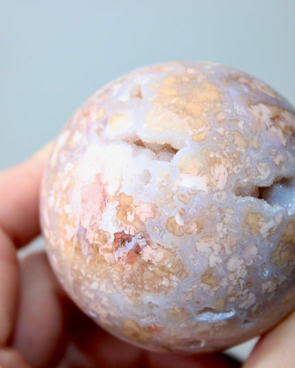 Elevate your space with the calming beauty and gentle energy of this hand-polished Flower Agate Sphere, a natural work of art that inspires peace, growth, and intention. Featuring dreamy shades of soft pink, creamy white, and warm peach, each sphere showcases unique floral-like inclusions that resemble delicate blooms suspended within the stone—making every piece truly one of a kind.