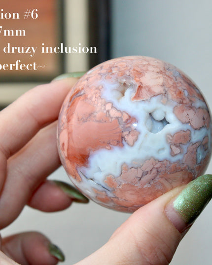 Elevate your space with the calming beauty and gentle energy of this hand-polished Flower Agate Sphere, a natural work of art that inspires peace, growth, and intention. Featuring dreamy shades of soft pink, creamy white, and warm peach, each sphere showcases unique floral-like inclusions that resemble delicate blooms suspended within the stone—making every piece truly one of a kind.