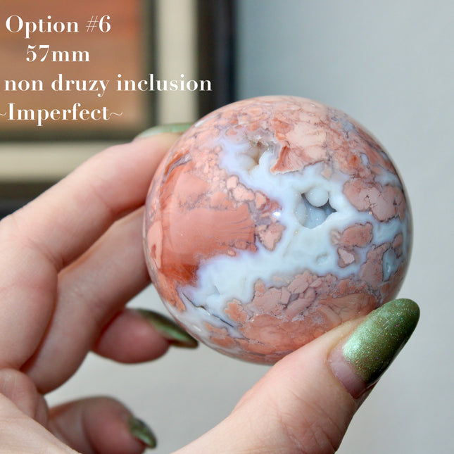 Elevate your space with the calming beauty and gentle energy of this hand-polished Flower Agate Sphere, a natural work of art that inspires peace, growth, and intention. Featuring dreamy shades of soft pink, creamy white, and warm peach, each sphere showcases unique floral-like inclusions that resemble delicate blooms suspended within the stone—making every piece truly one of a kind.