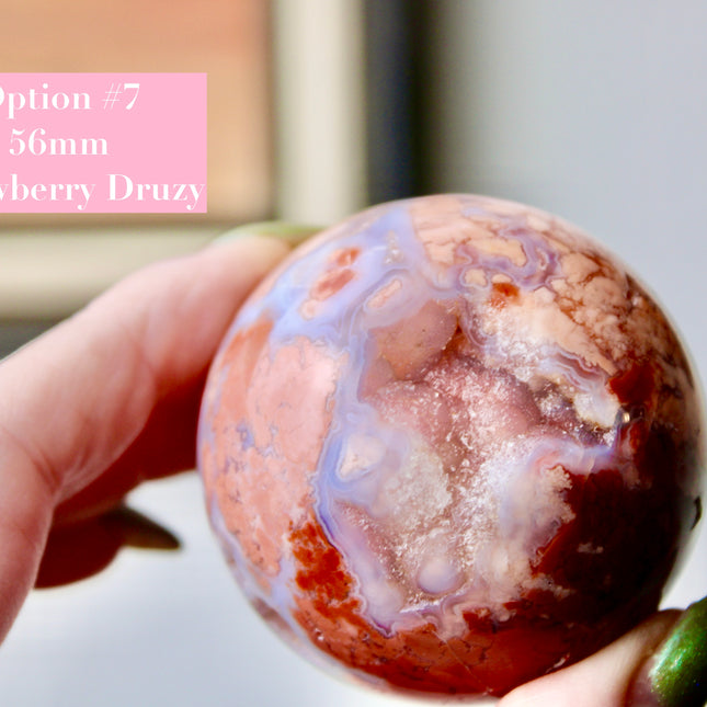 Elevate your space with the calming beauty and gentle energy of this hand-polished Flower Agate Sphere, a natural work of art that inspires peace, growth, and intention. Featuring dreamy shades of soft pink, creamy white, and warm peach, each sphere showcases unique floral-like inclusions that resemble delicate blooms suspended within the stone—making every piece truly one of a kind.