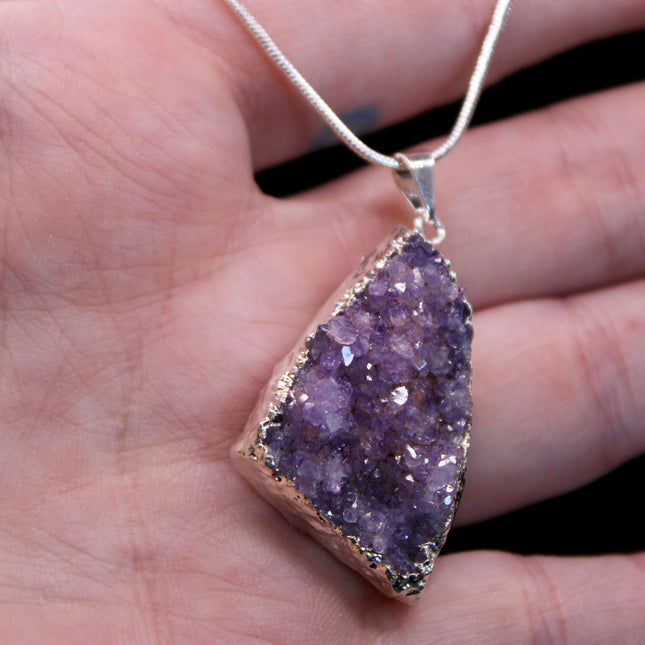 A beautiful Amethyst Pendant hangs gracefully from a sleek silver-color chain, combining natural elegance with everyday wearability. The pendant features a polished amethyst point or cabochon (style can vary), showcasing rich purple hues with subtle marbling or translucence that catches the light. Set in a simple metal cap or loop, the natural stone takes center stage. The silver-tone chain adds a modern, minimalist touch and pairs effortlessly with any outfit.