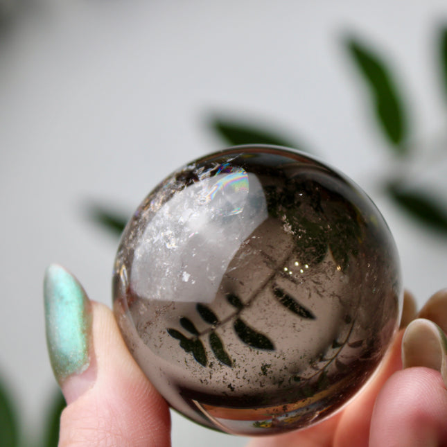 High grade genuine smoky quartz crystal sphere with natural clarity in deep translucent brown to smoky gray tones, hand-polished and displayed on a sturdy silver stand – grounding crystal for meditation, energy clearing, and root chakra healing