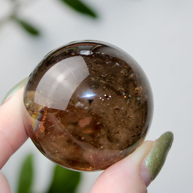 High grade genuine smoky quartz crystal sphere with natural clarity in deep translucent brown to smoky gray tones, hand-polished and displayed on a sturdy silver stand – grounding crystal for meditation, energy clearing, and root chakra healing