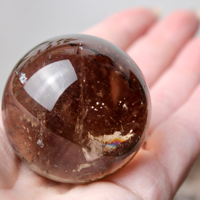 High grade genuine smoky quartz crystal sphere with natural clarity in deep translucent brown to smoky gray tones, hand-polished and displayed on a sturdy silver stand – grounding crystal for meditation, energy clearing, and root chakra healing