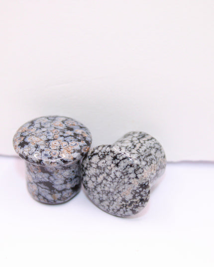 These Snowflake Obsidian Double Flared Plugs feature a smooth, polished surface with natural gray-white crystal "snowflakes" scattered across a rich black volcanic glass base. The double flare ensures a secure, comfortable fit for stretched ears without the need for O-rings. Each pair is uniquely patterned, showcasing the stone’s natural beauty and grounding energy. Durable and stylish, these plugs add a bold yet refined touch to any stretched ear jewelry collection.