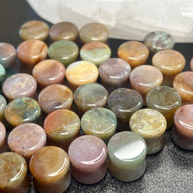 A beautifully varied pair of Rainbow Indian Agate Plugs rests on a natural-toned background, each plug showcasing its own unique mix of earthy colors. From deep forest green and mossy olive to warm rust, cream, and occasional hints of burgundy or gray, the natural banding and marbling of the stone give these plugs a one-of-a-kind character. The polished surface brings out the rich tones and subtle textures of the agate. Shaped with a comfortable, secure double flare, these plugs are perfect for those who ap