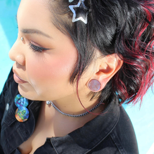 A beautifully varied pair of Rainbow Indian Agate Plugs rests on a natural-toned background, each plug showcasing its own unique mix of earthy colors. From deep forest green and mossy olive to warm rust, cream, and occasional hints of burgundy or gray, the natural banding and marbling of the stone give these plugs a one-of-a-kind character. The polished surface brings out the rich tones and subtle textures of the agate. Shaped with a comfortable, secure double flare, these plugs are perfect for those who ap