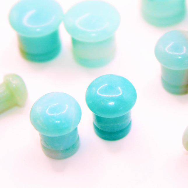 A beautifully fossilized pair of Ammonite Single Flare Plugs rests on a warm-toned background, showcasing the intricate spiral patterns of ancient marine life. Each plug is carefully carved from real ammonite fossils, revealing natural chambers in warm shades of caramel, amber, and deep brown, sometimes accented with hints of iridescent sheen. The surface is smoothly polished, allowing the fossil’s unique structure to shine through. Designed with a single flare and fitted with O-rings, these plugs offer a s