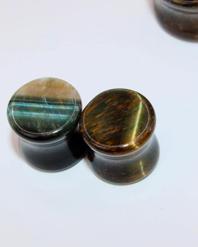 A sleek and polished pair of Blue Tiger Eye plugs, also known as Falcon’s Eye, radiating deep shades of midnight blue, slate, and hints of black. Each plug features the signature chatoyancy of the stone—a silky, light-catching shimmer that moves across the surface as it shifts in the light. The smooth, double-flared design offers both comfort and style, with each plug showcasing natural banding and a unique pattern.